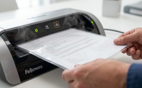 Person inserting document inside thermal laminating pouch into machine.